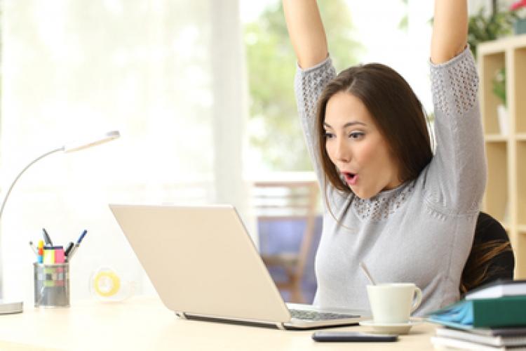 An excited woman with her arms up while looking at her laptop